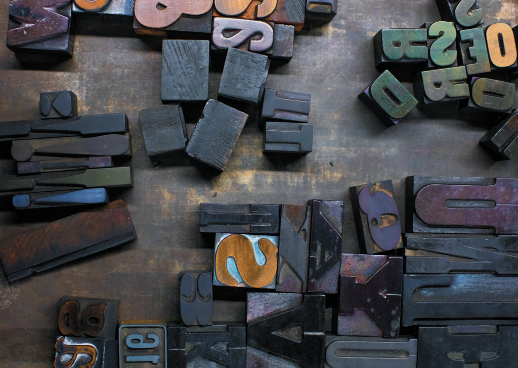 Justin Tsucalas An aerial view of wooden letter stamps on a wooden table. The stamps are all made from a dark wood and show different letters.